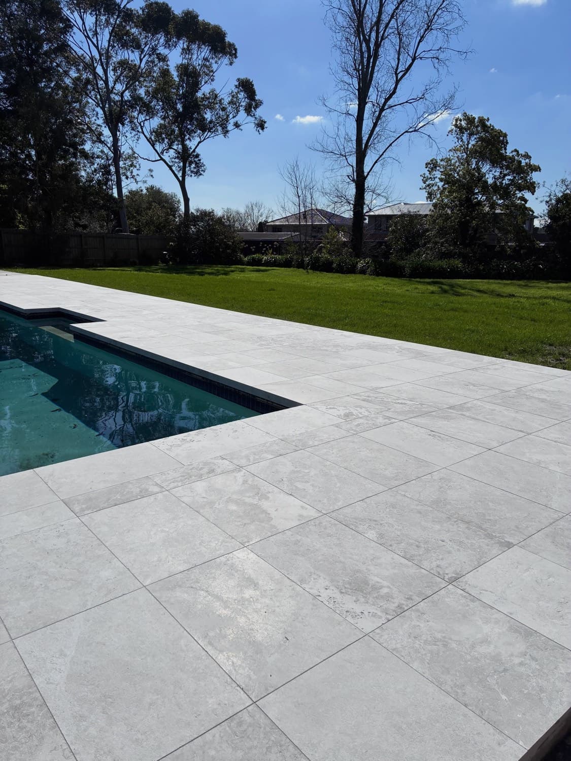 Large-format stone paving running along the edge of a swimming pool, with lawn and gum trees behind