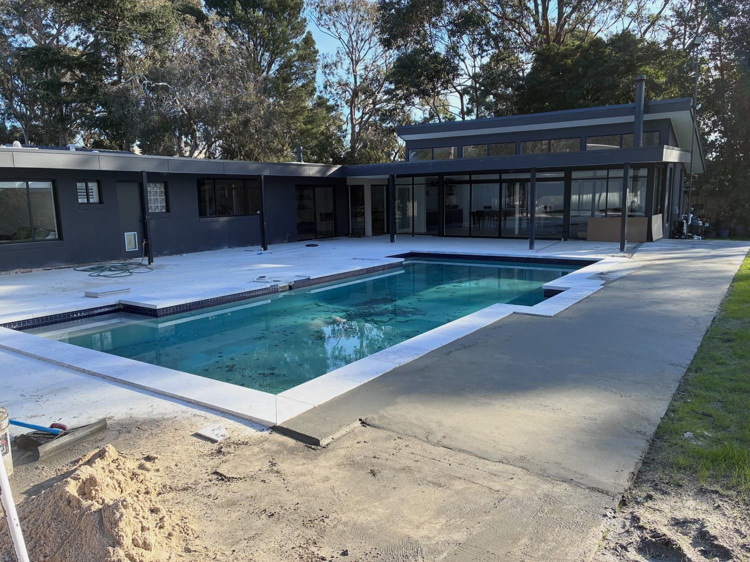 Pale stone paving laid around a swimming pool beside a new single-storey house