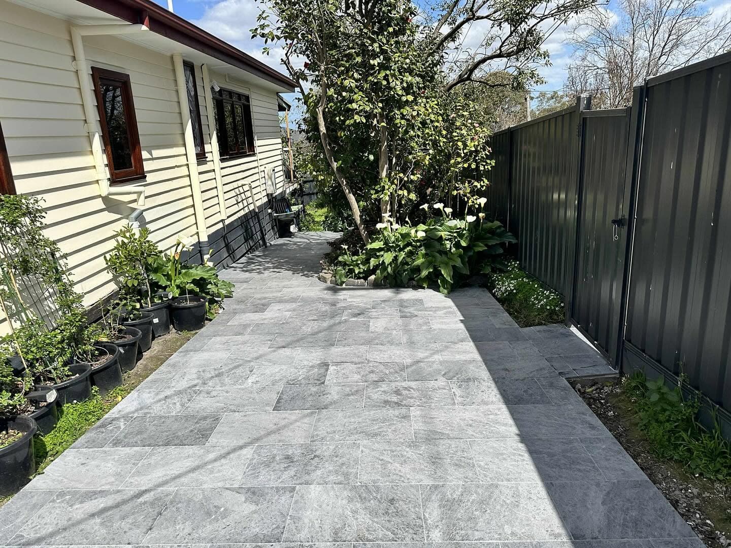 Grey stone paving path running between a weatherboard house and a planted garden bed
