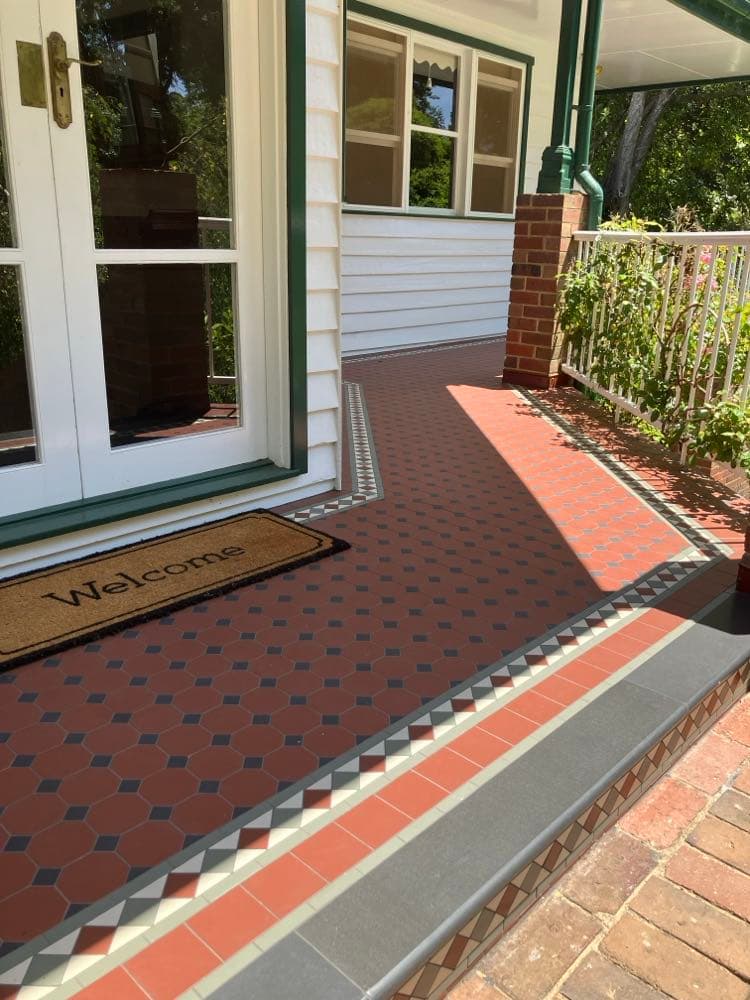 Tessellated verandah tiling in red, black and cream running to a front door with a doormat on it