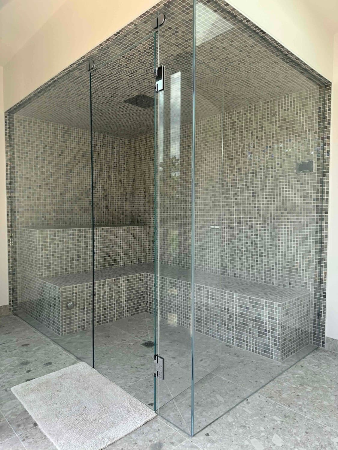 Frameless glass shower with a built-in bench seat, tiled in pale speckled stone