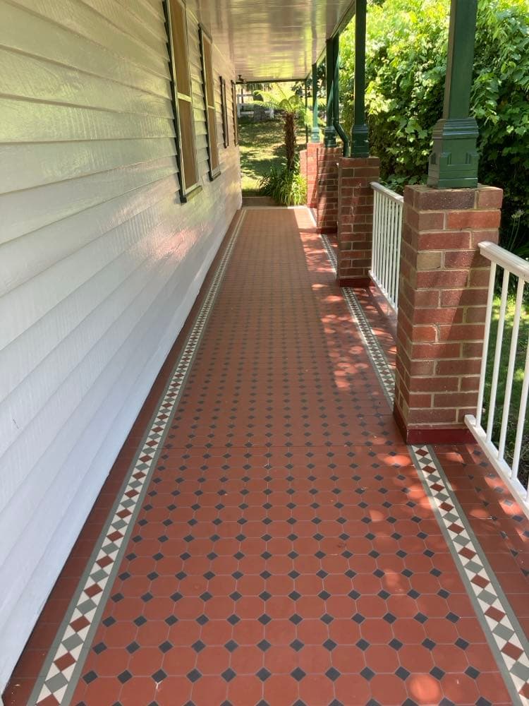 Red tessellated verandah tiles with a patterned border, running the length of a weatherboard house between brick piers