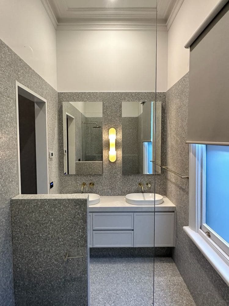 Bathroom with grey stone-look wall tiles, twin basins under two mirrors and a speckled floor